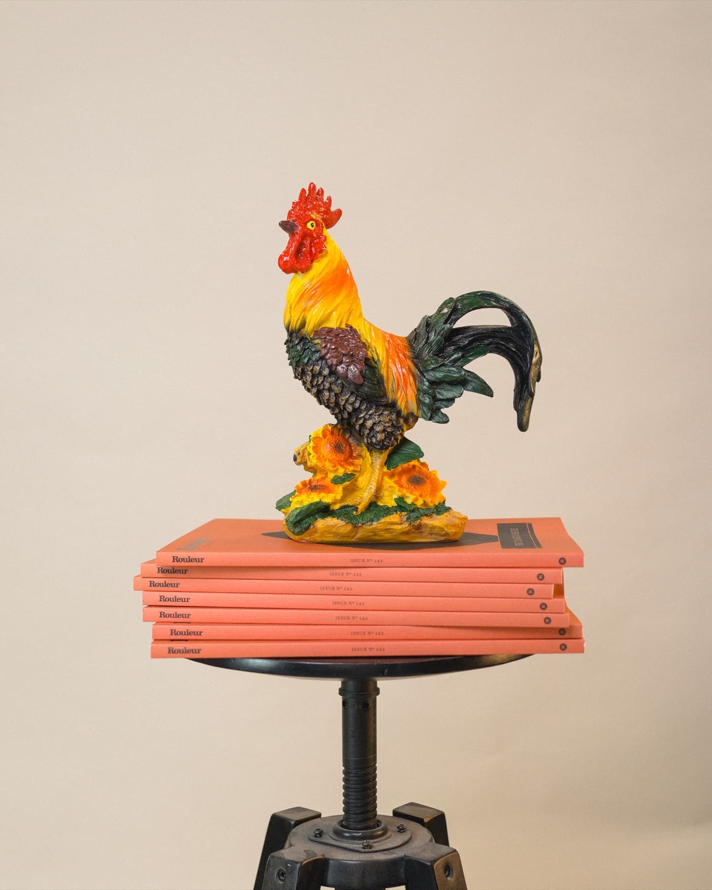 A rooster ornament perched on a stack of Rouleur magazines